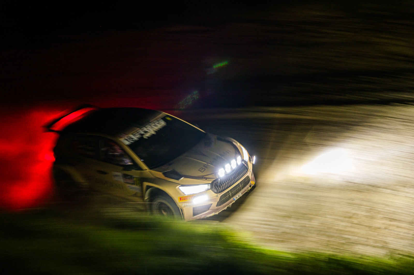 Un'auto da rally di notte, i fari accesi nella polvere illuminata