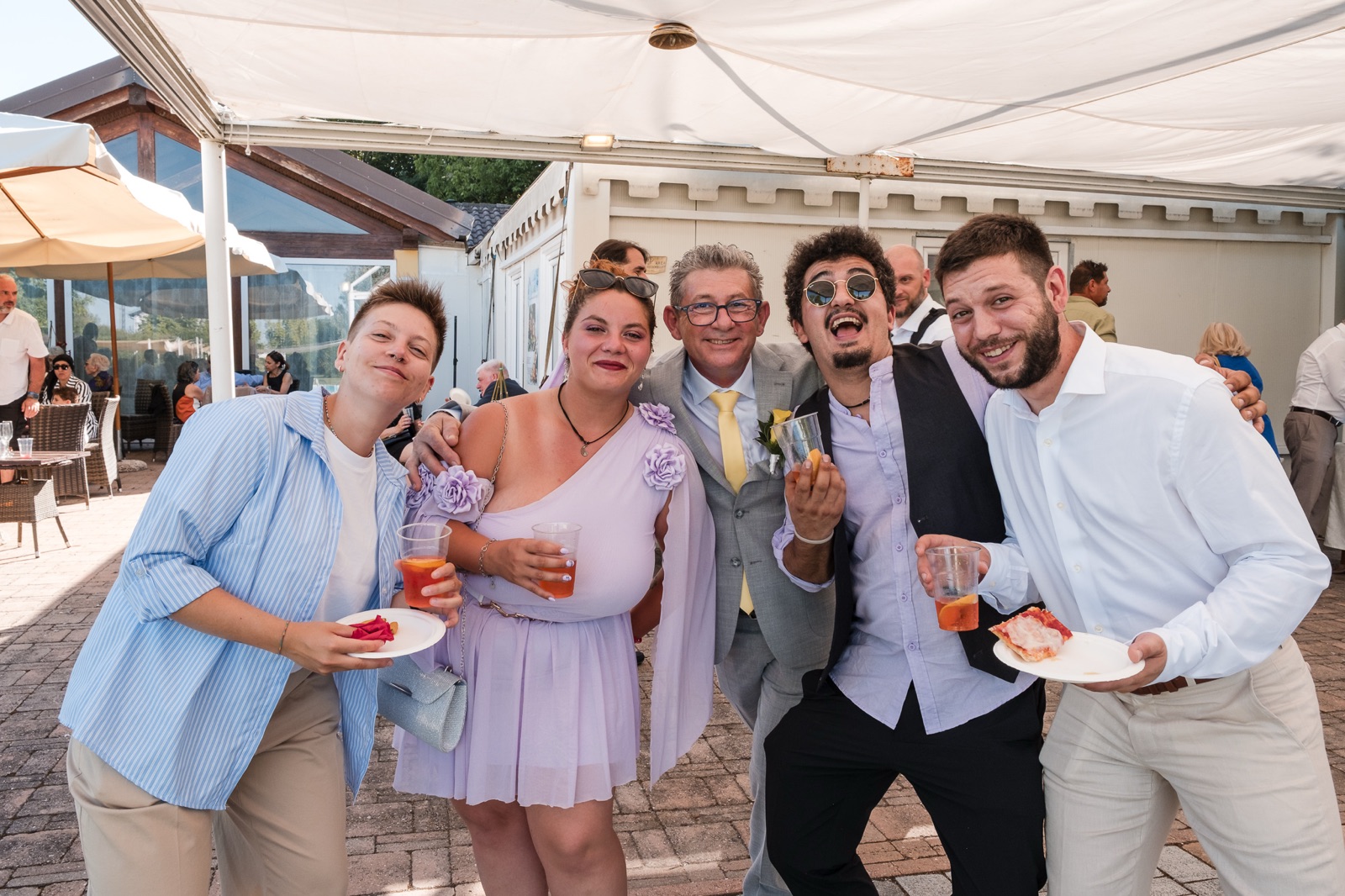 Un gruppo di invitati ride sotto il gazebo, bicchieri e piatti in mano